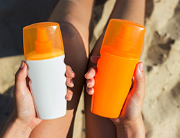 Hands hold two sunscreen bottles.